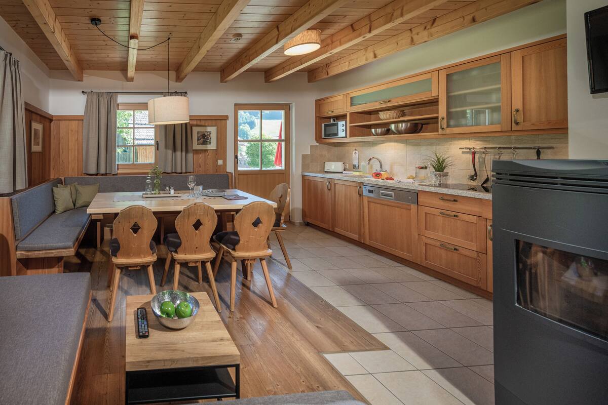 Une cuisine moderne avec des meubles en bois, un coin repas doté d’un banc et un four encastré.