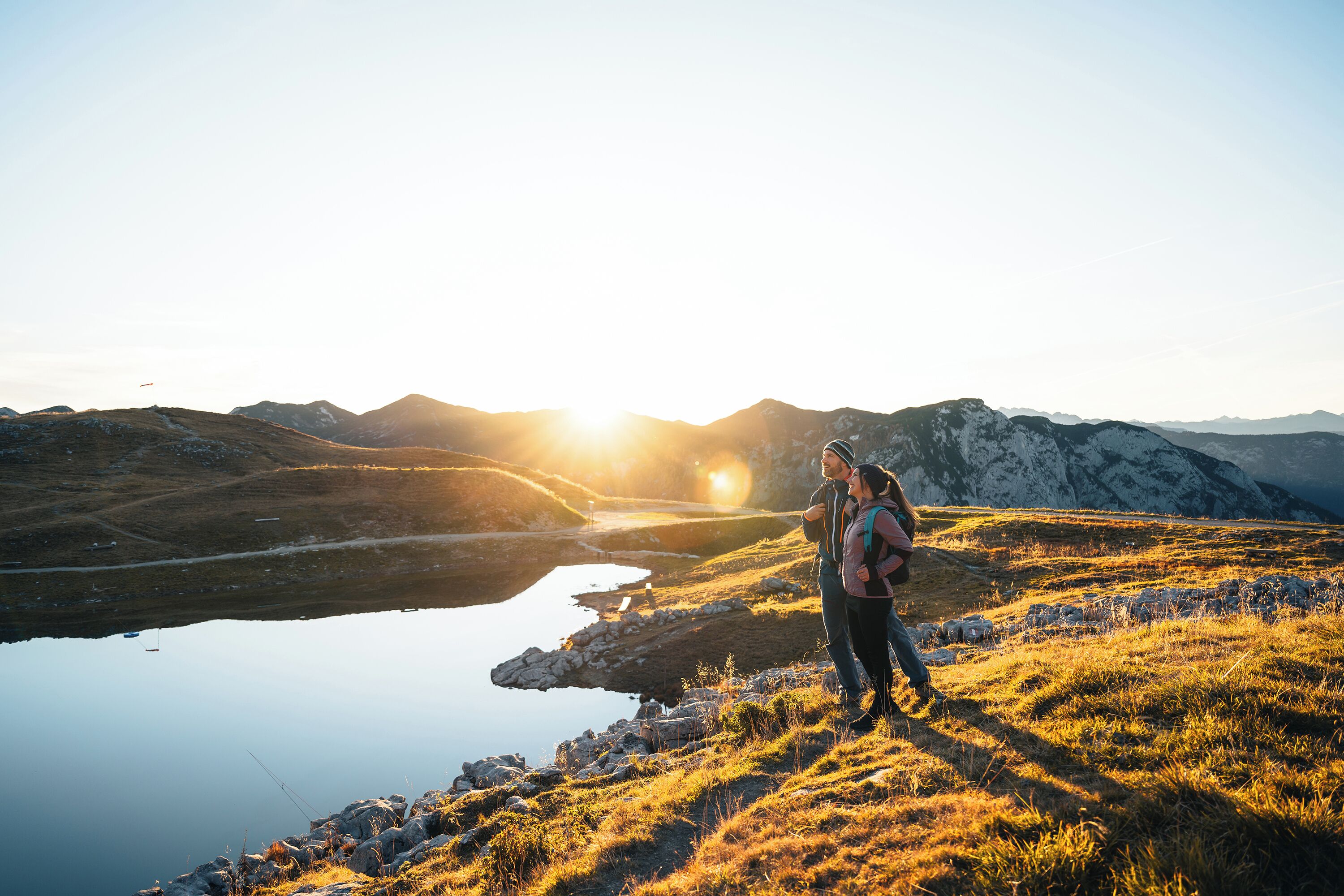 Une personne se tient sur une colline herbeuse, d’où elle domine un lac paisible, avec des montagnes en arrière-plan.