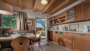 A kitchen with wooden cabinets, a dining table with chairs, and a view of the outdoors. - AlpenParks Hagan Lodge Altaussee (Altaussee)