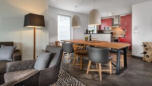 Una sala de estar moderna con un sofá, una mesa de comedor con sillas y una zona de cocina con armarios rojos y un microondas.