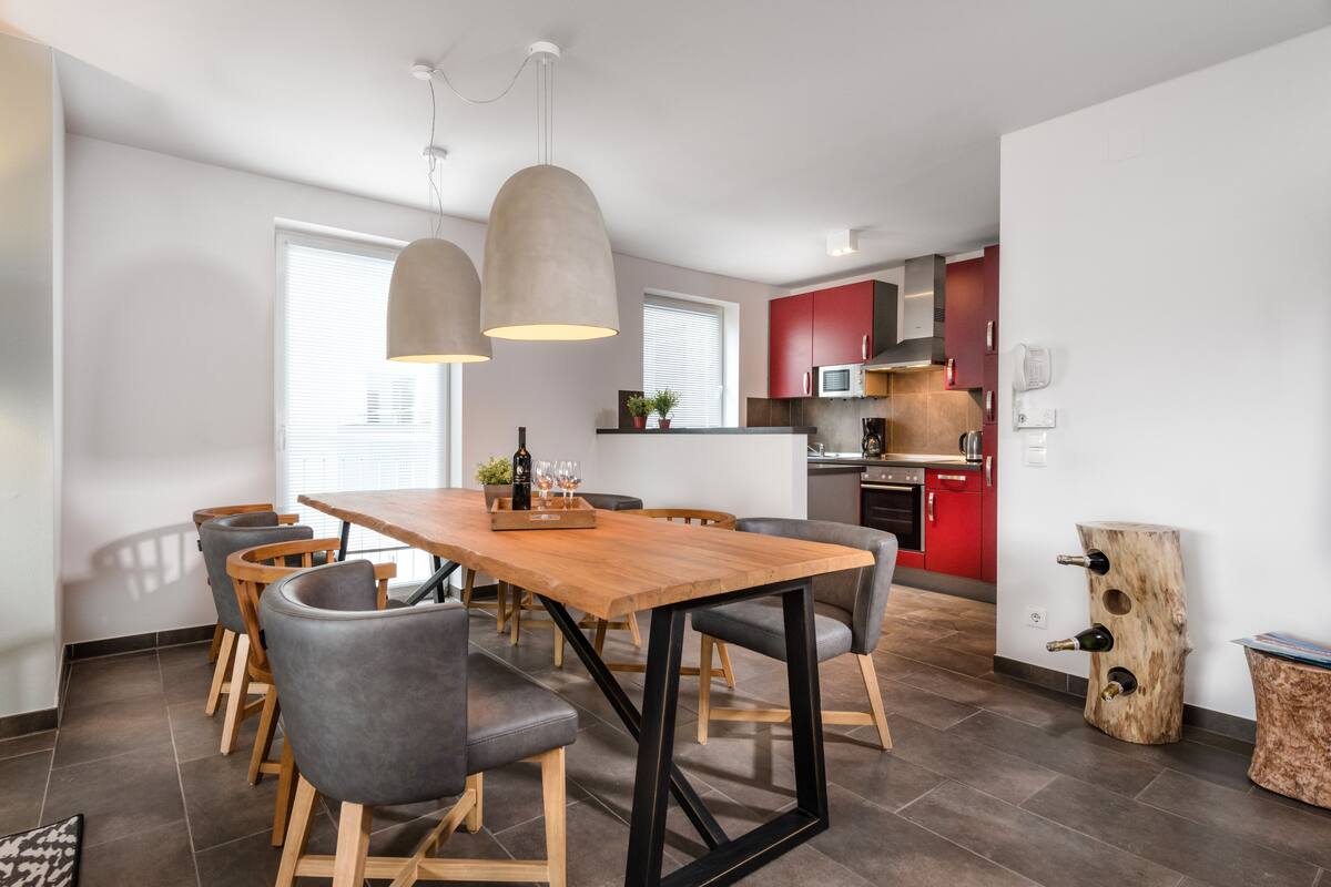 Una cocina moderna con gabinetes rojos, una mesa de comedor de madera y sillas grises.