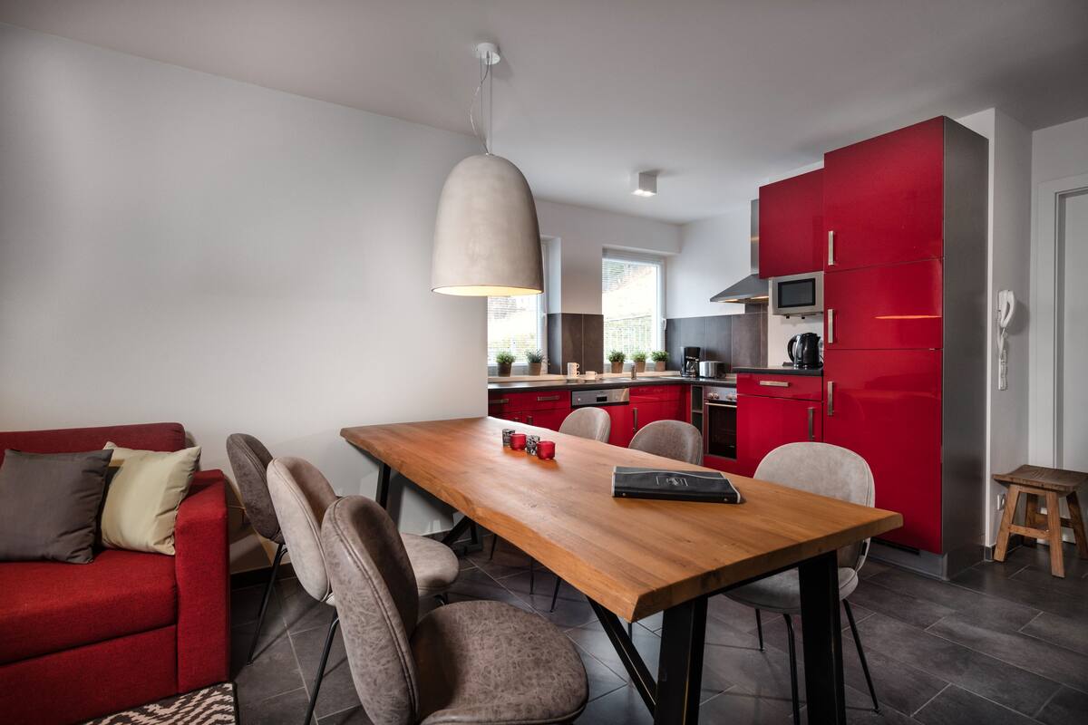 Una cocina moderna con armarios rojos, una mesa de comedor de madera y un sofá rojo.