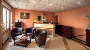 A reception area with a reception desk, two leather chairs, a coffee table, a potted plant, and a painting on the wall. - Hotel Neptune (Paris)
