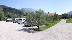 A parking area with several cars, a gravel path leading to a building, and mountains in the background. - Agritur La Cort (Arco)