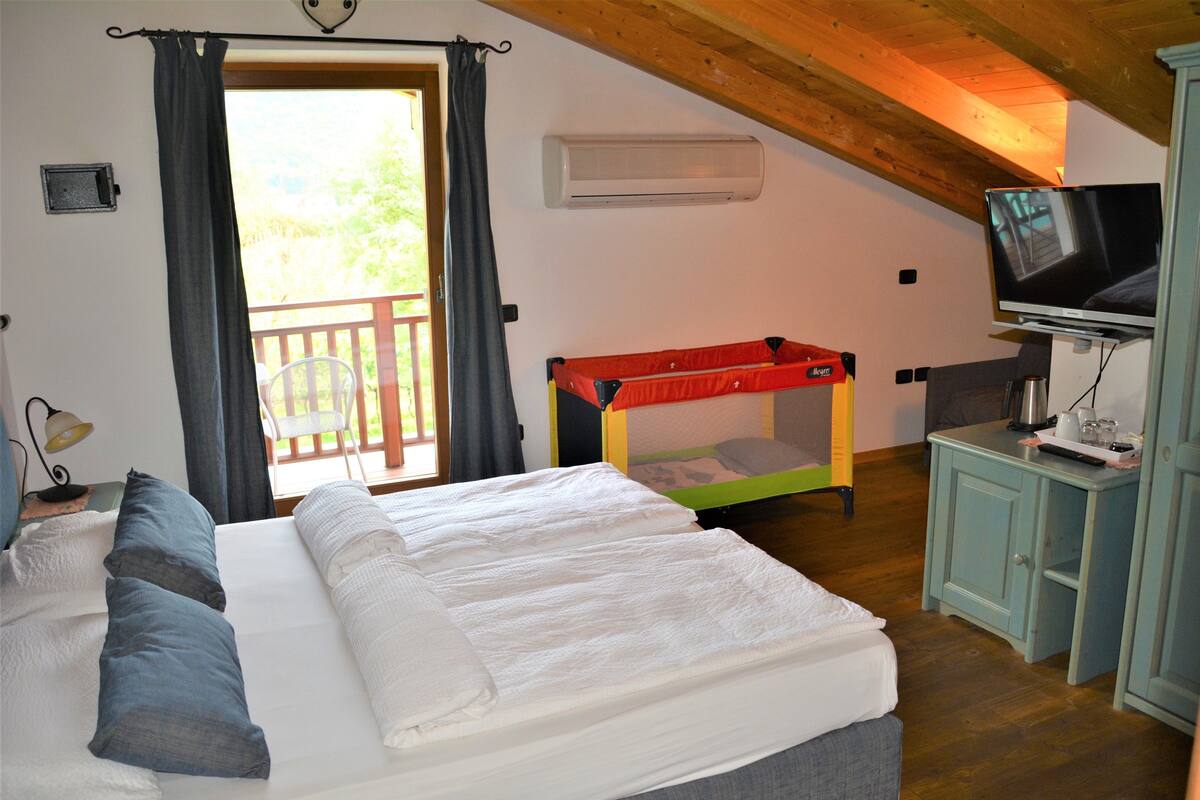 Un dormitorio con una cama, televisor, una mesita y una ventana con cortinas.