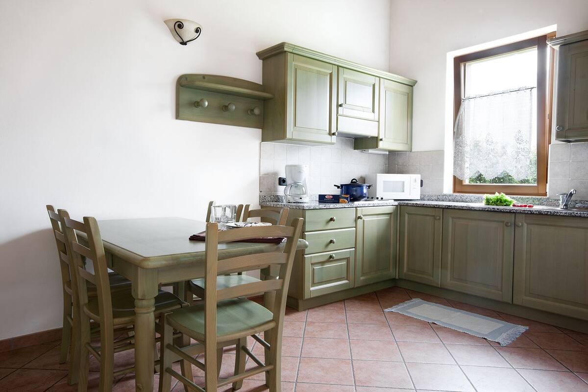 Una cocina con una mesa de comedor, sillas, armarios, un microondas y una ventana con vistas.