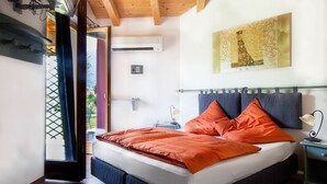 A bedroom with a bed, a nightstand, a wall-mounted air conditioner, and a window with a view of greenery. - Agritur La Cort (Arco)