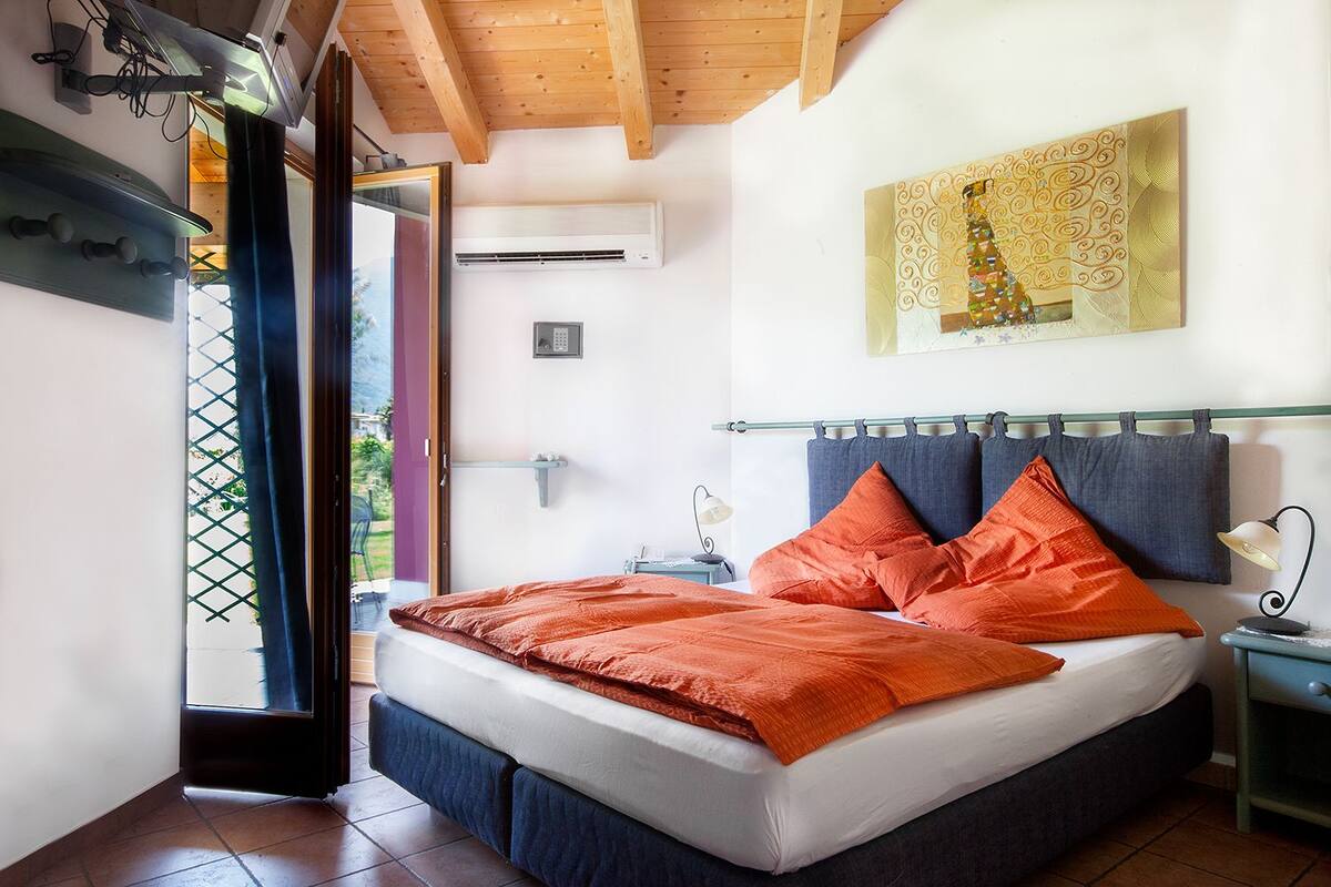 Un dormitorio con cama, mesita de noche, aire acondicionado en la pared y ventana con vista a zonas verdes.