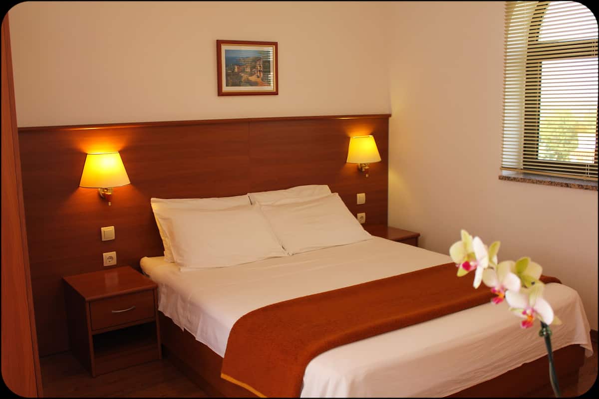 A neatly made bed with white linens, two bedside lamps, a nightstand, and a framed picture on the wall.