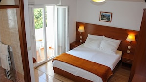 A hotel room with a bed, two bedside lamps, a wooden headboard, a picture on the wall, and a sliding glass door leading to an outdoor area. - Gargamelo Pension (Porec)