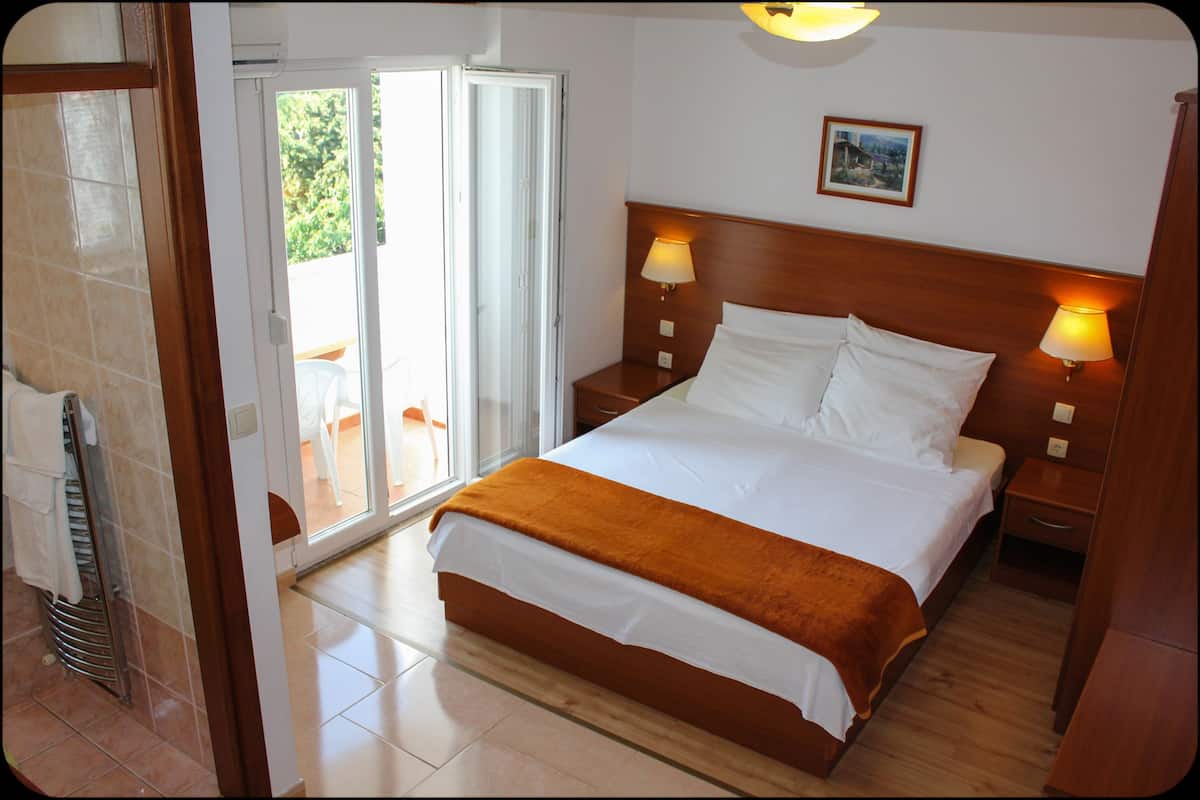 A hotel room with a bed, two bedside lamps, a wooden headboard, a picture on the wall, and a sliding glass door leading to an outdoor area.