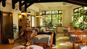 A restaurant with wooden tables and chairs, a stone wall, and large windows with plants. - Gargamelo Pension (Porec)