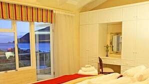 A bedroom with a large bed, a window with curtains, and a view of the sea.