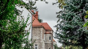 Een gebouw van steen met een rood dak, omgeven door groen en een geplaveid pad.