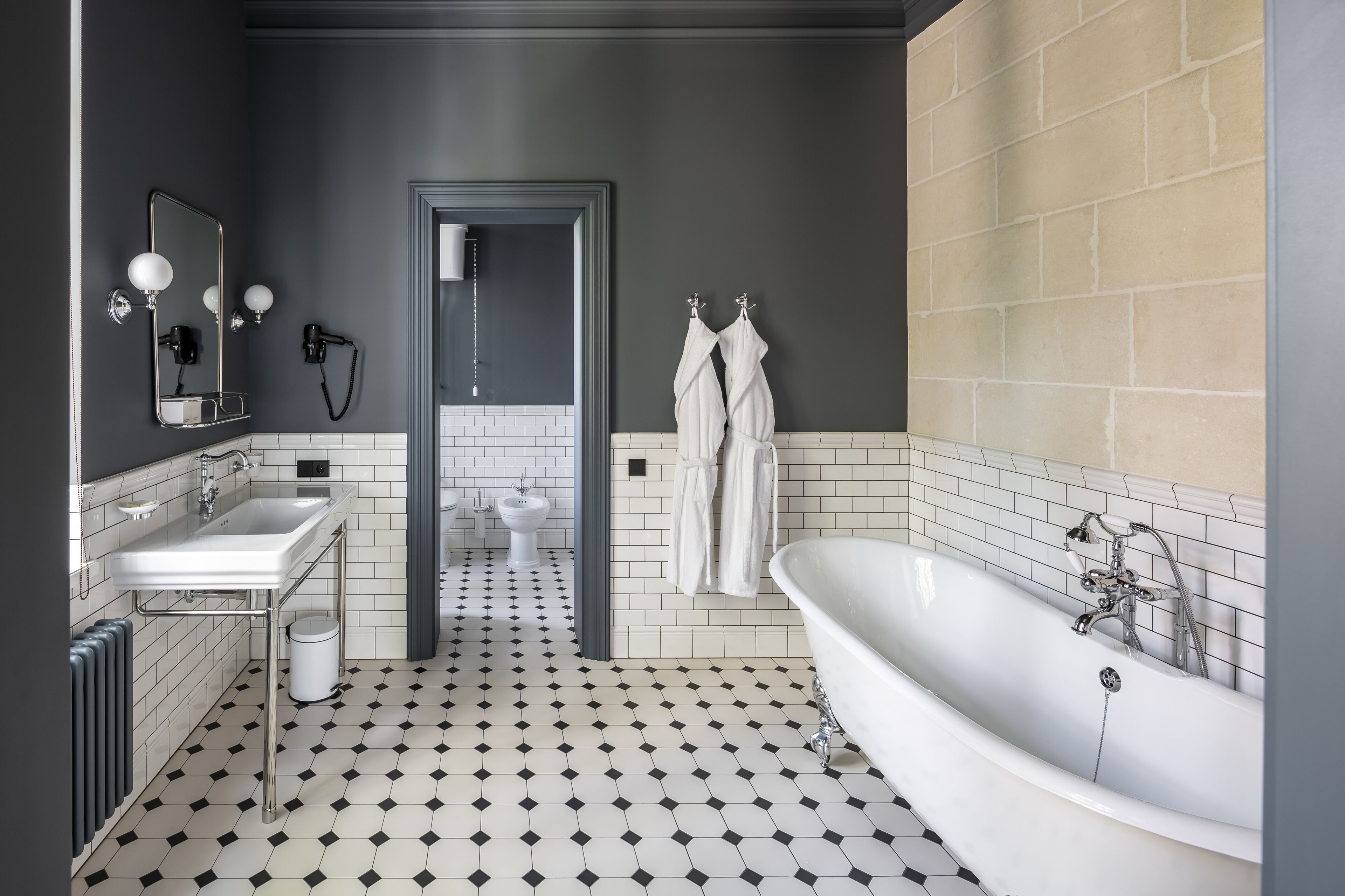 Un baño moderno con suelo de baldosas blanco y negro, un lavamanos blanco, una bañera grande y un espejo con luces.