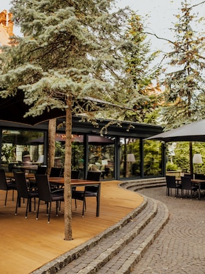 An outdoor seating area with tables and chairs, surrounded by trees and a cobblestone path. - Lion's Castle (Lviv)