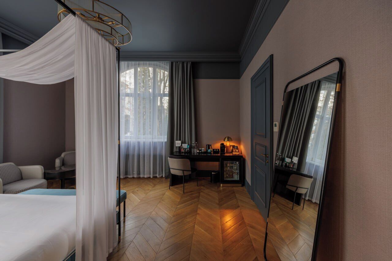 Een slaapkamer met hemelbed, bureau met lamp, spiegel en uitzicht op het omliggende landschap.