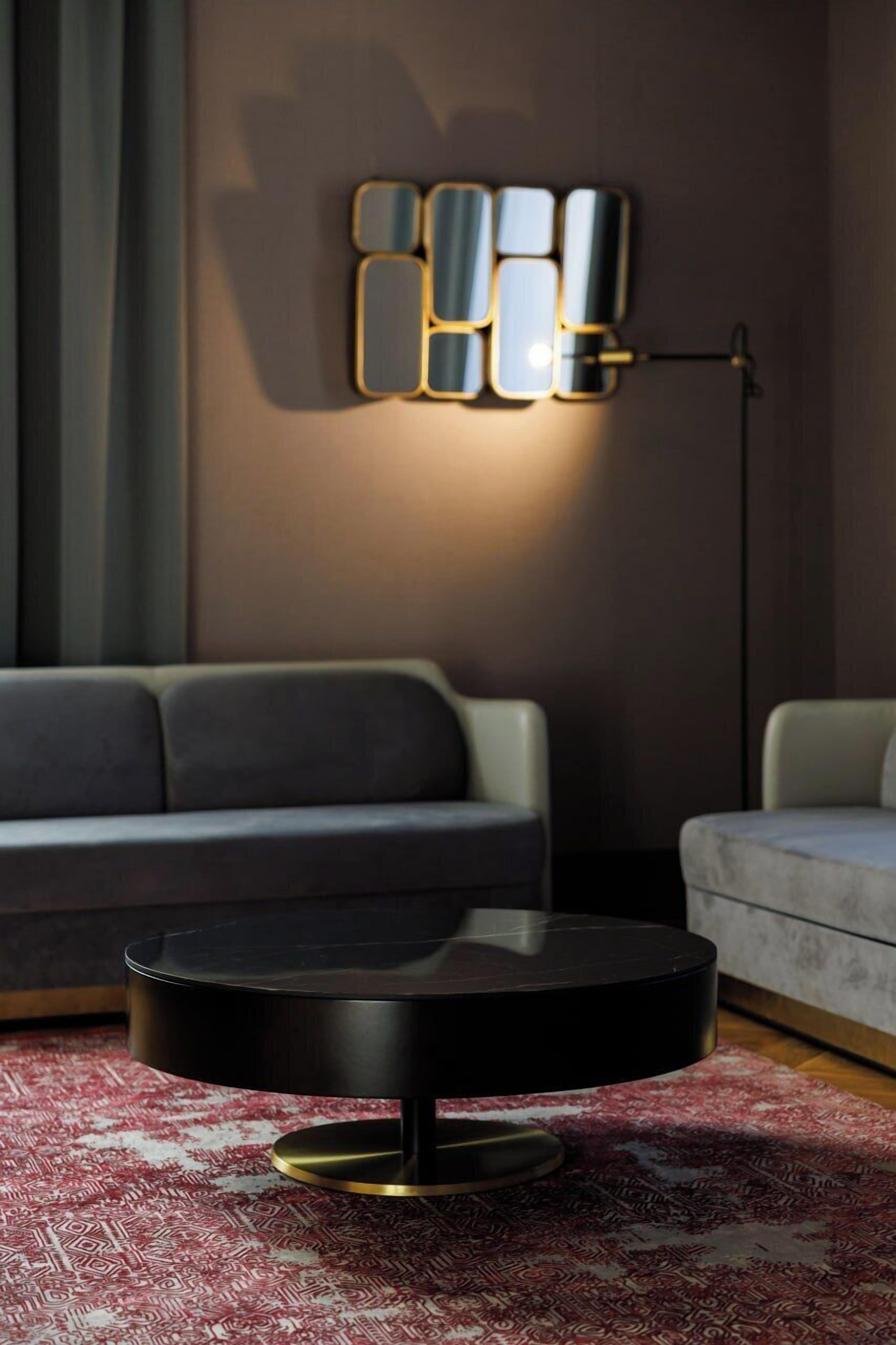 A modern living room with a round black coffee table, a patterned rug, a sofa, and a floor lamp with a geometric light fixture.