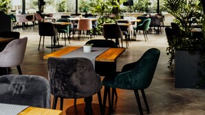 Een eethoek binnen met tafels, stoelen, hangende bolvormige lampen en potplanten.