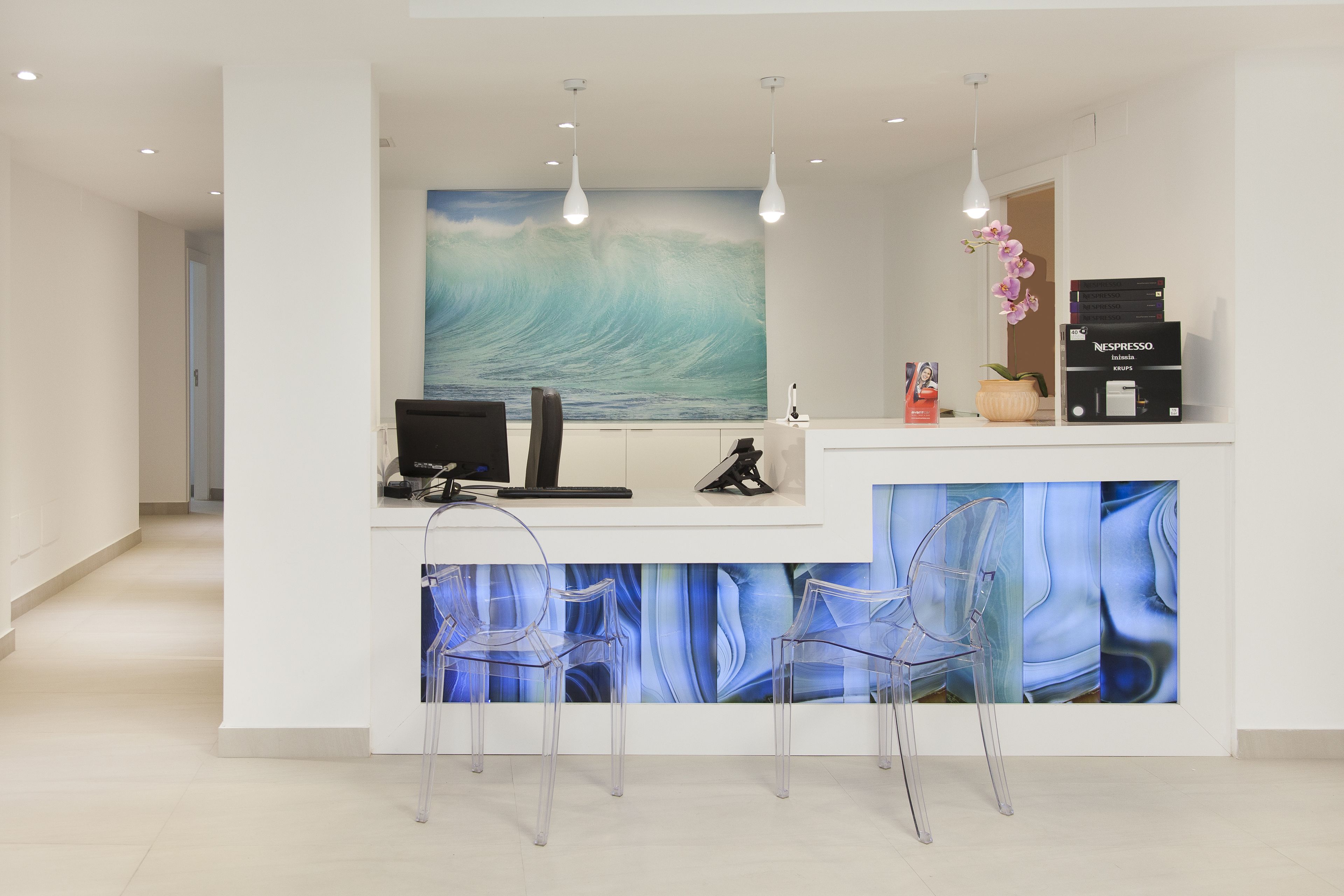 A reception area with a wave painting, clear chairs, a coffee machine, and a Nespresso machine.