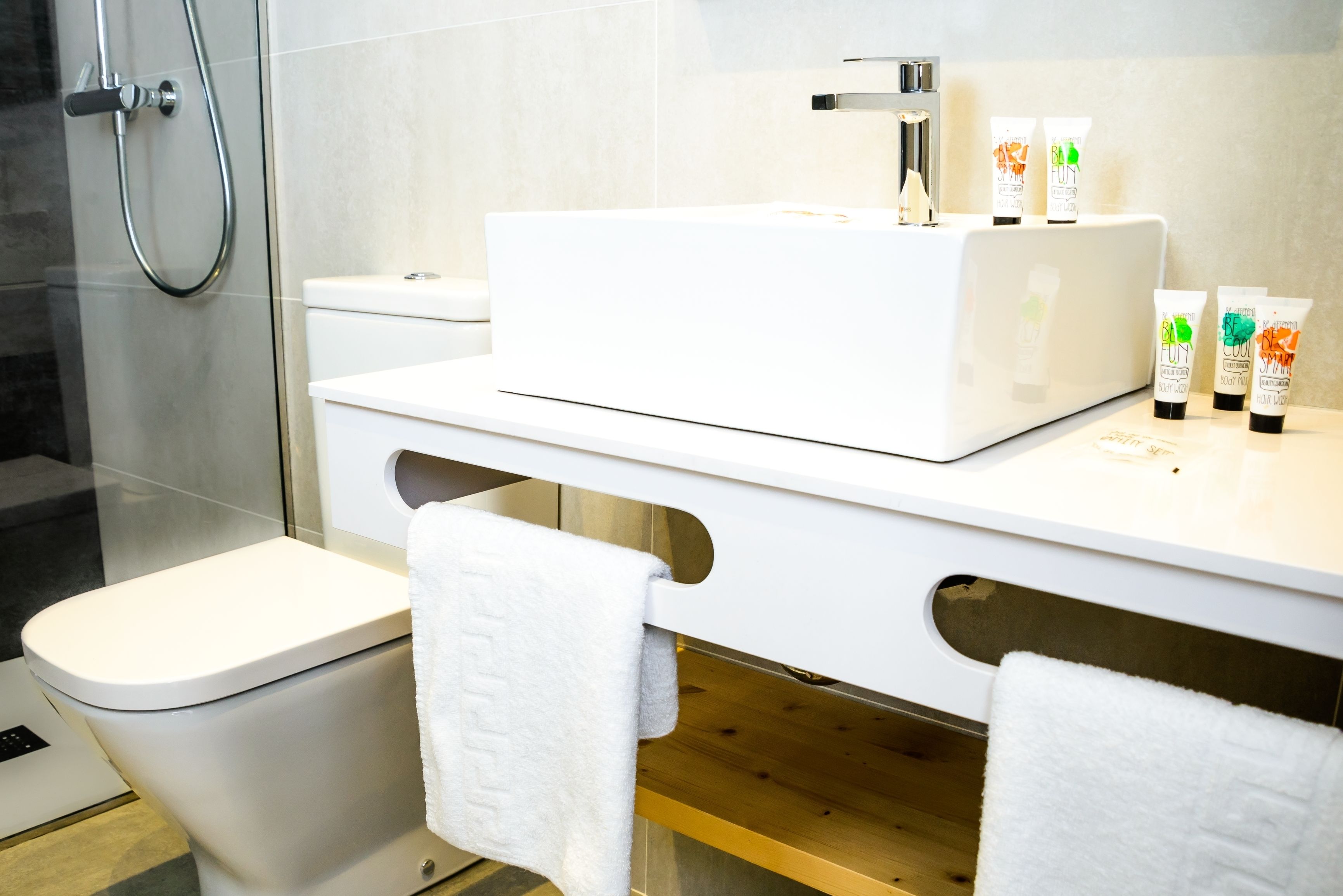 A modern bathroom with a white sink, toilet, and shower. There are three toiletries on the sink counter.