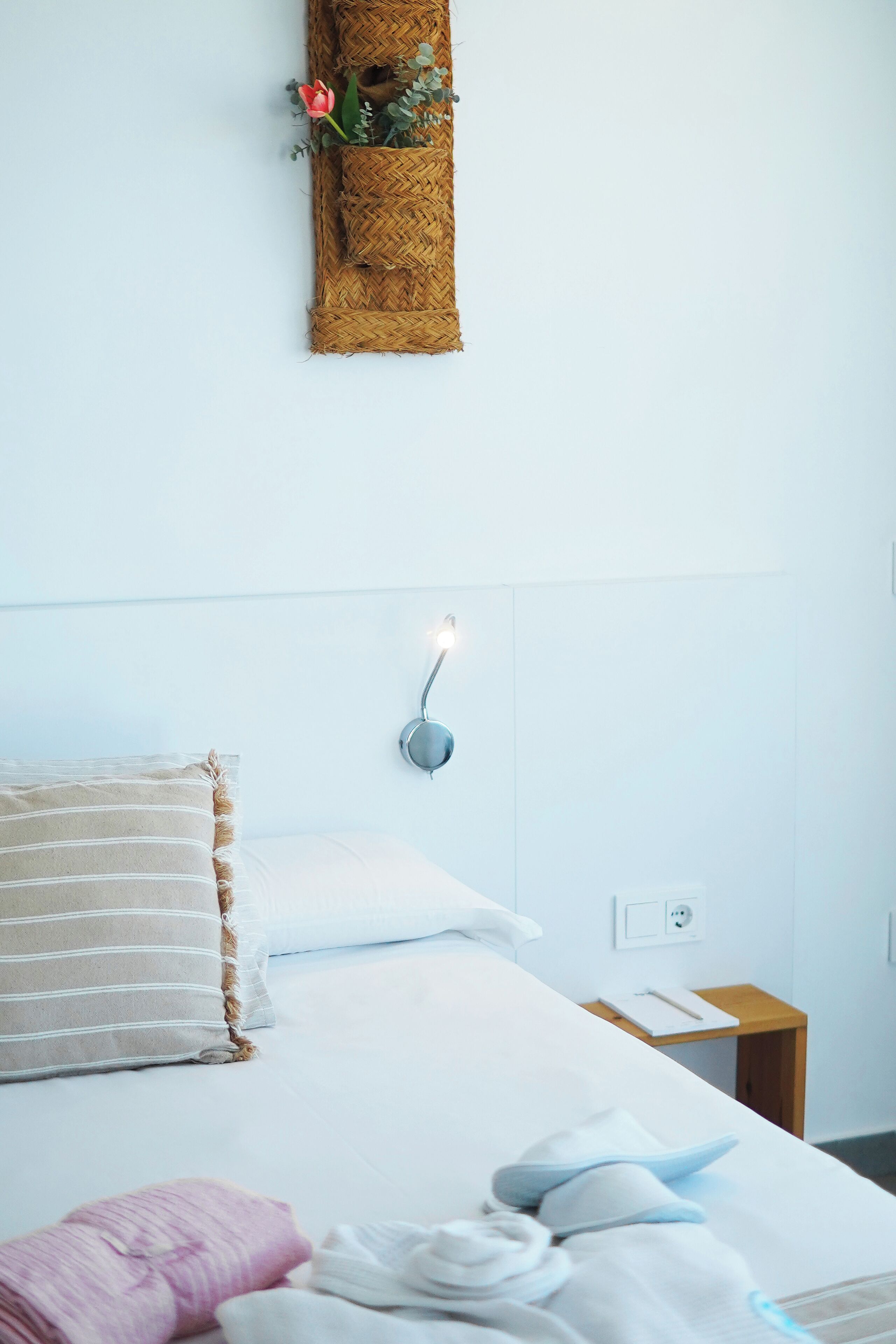 Un letto rifatto con cuscini a righe, un comodino con una lampada e una pianta sospesa al muro.