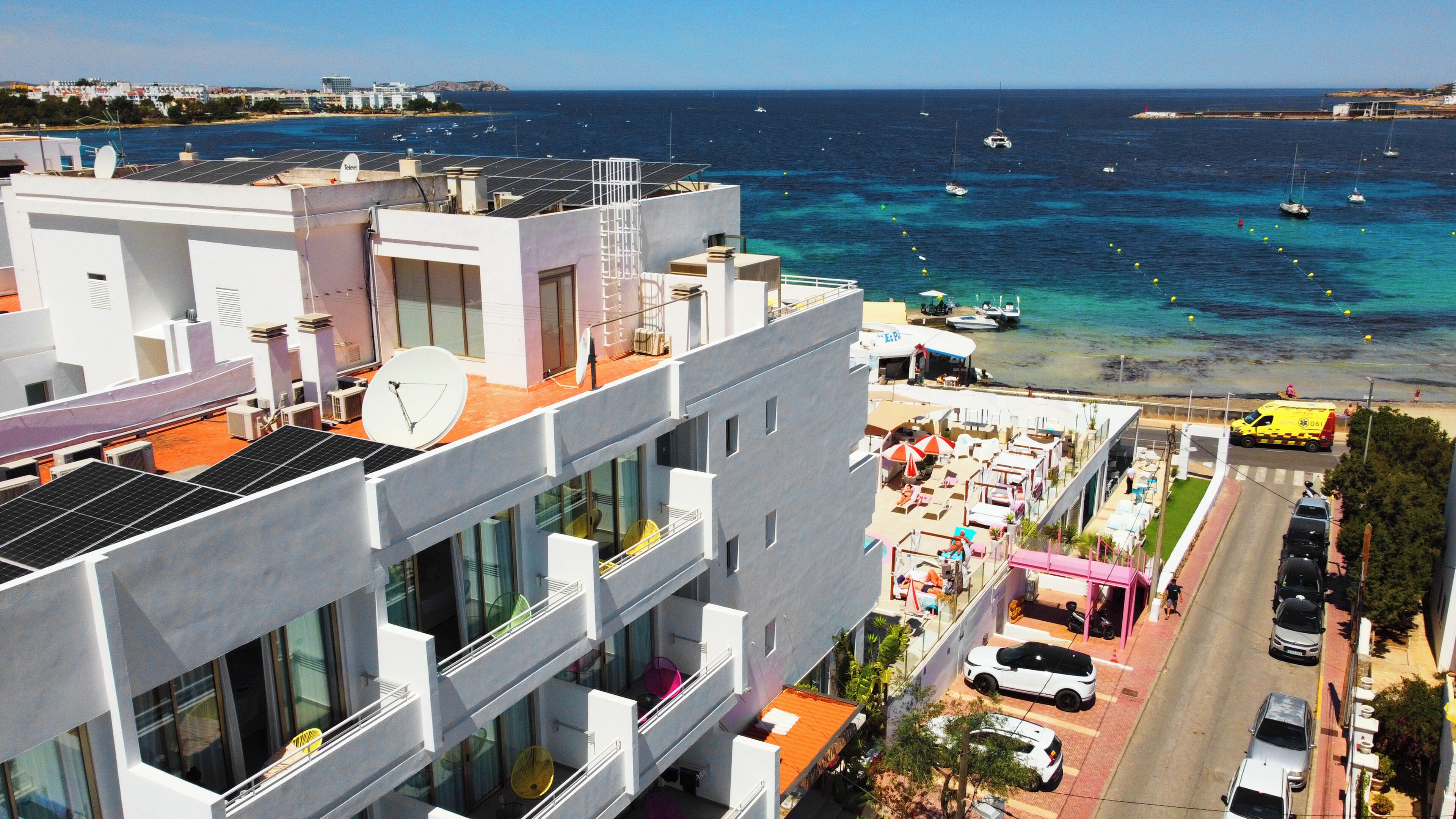 A modern building with multiple balconies overlooking a coastal area with boats and a clear sky.