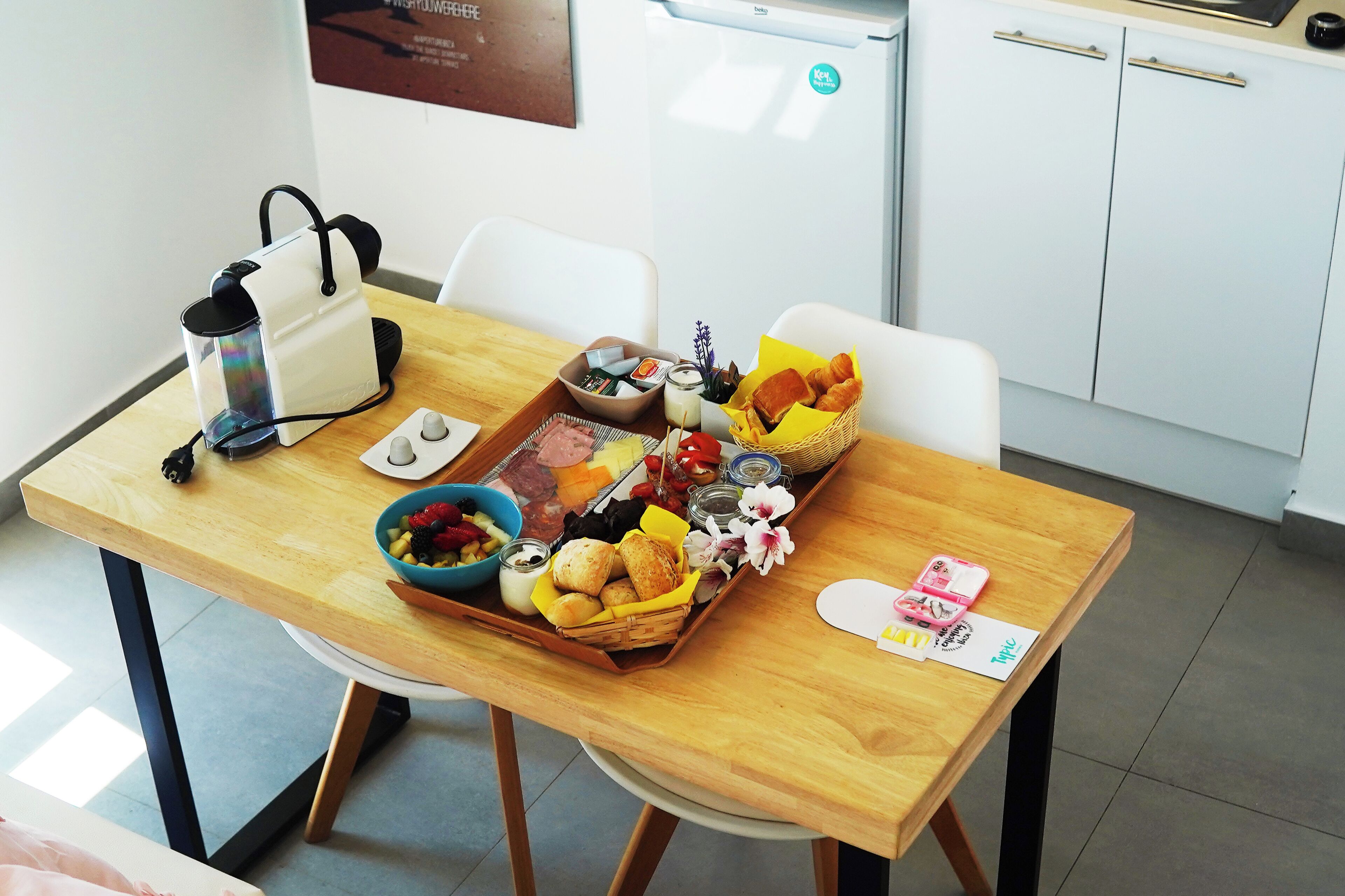 A dining table with a variety of food items, a coffee maker, and a basket of bread.