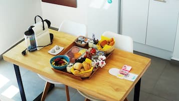 A dining table with a variety of food items, a coffee maker, and a basket of bread.