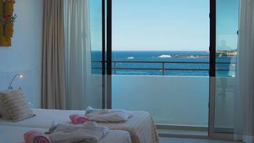 A hotel room with a bed, a nightstand, and a view of the sea through large windows.