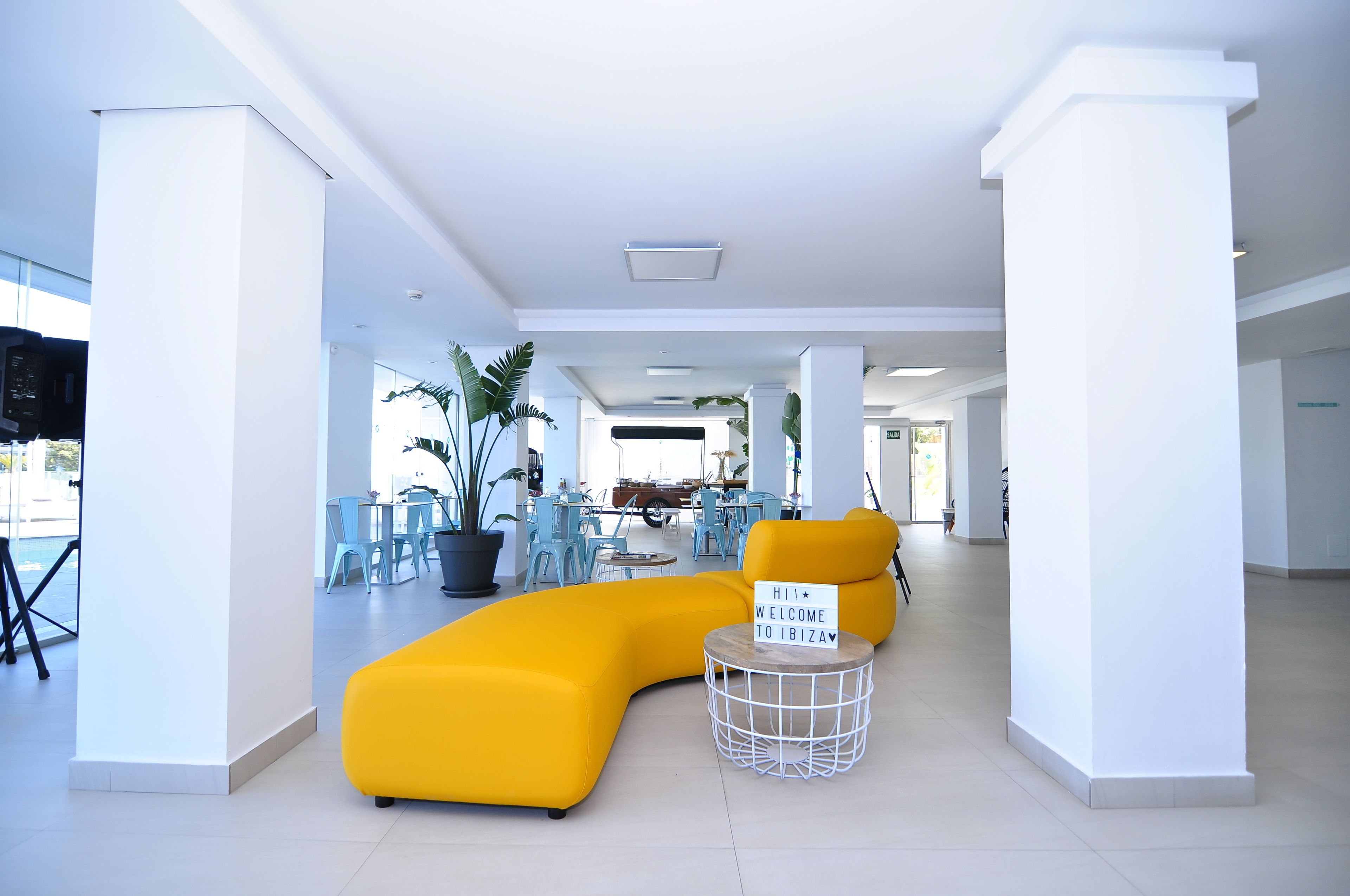 A spacious lobby with a yellow sectional sofa, a round coffee table, and a sign welcoming to Ibiza.