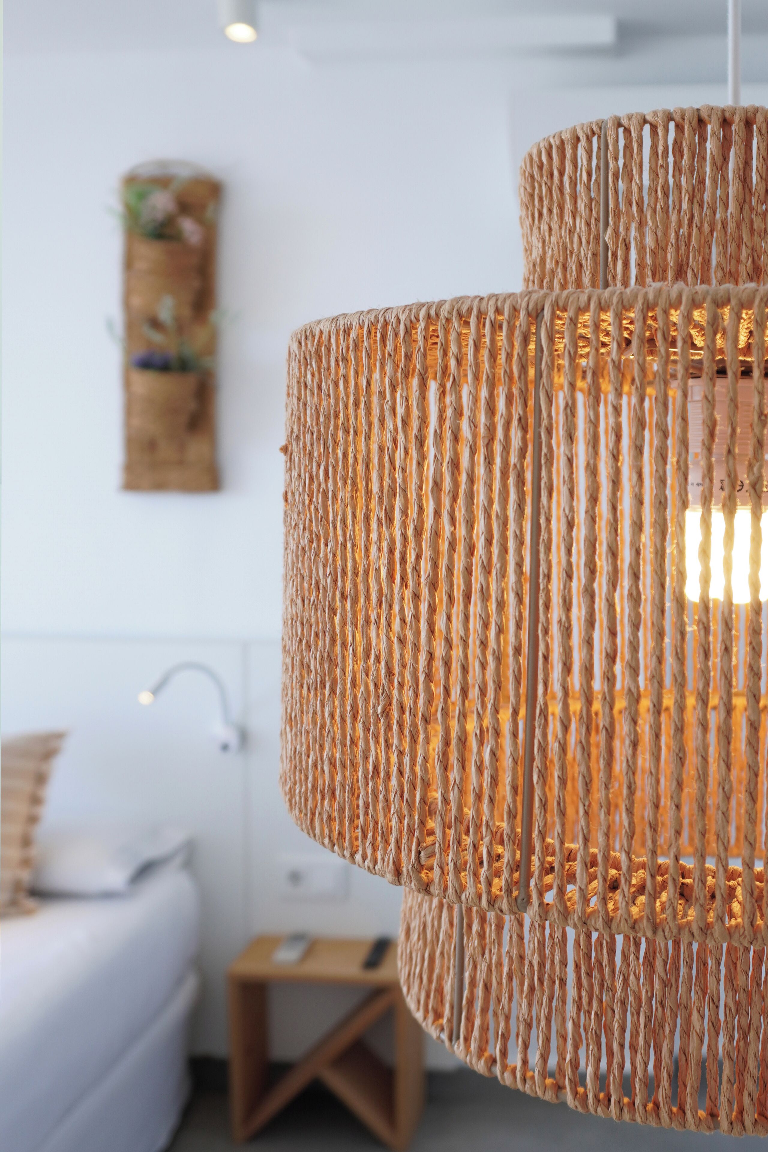 A wicker chandelier in a modern room with a white bed and a small wooden side table.