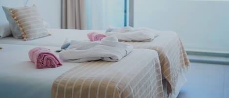 A hotel room with two beds, each with a striped bedspread and a rolled towel.