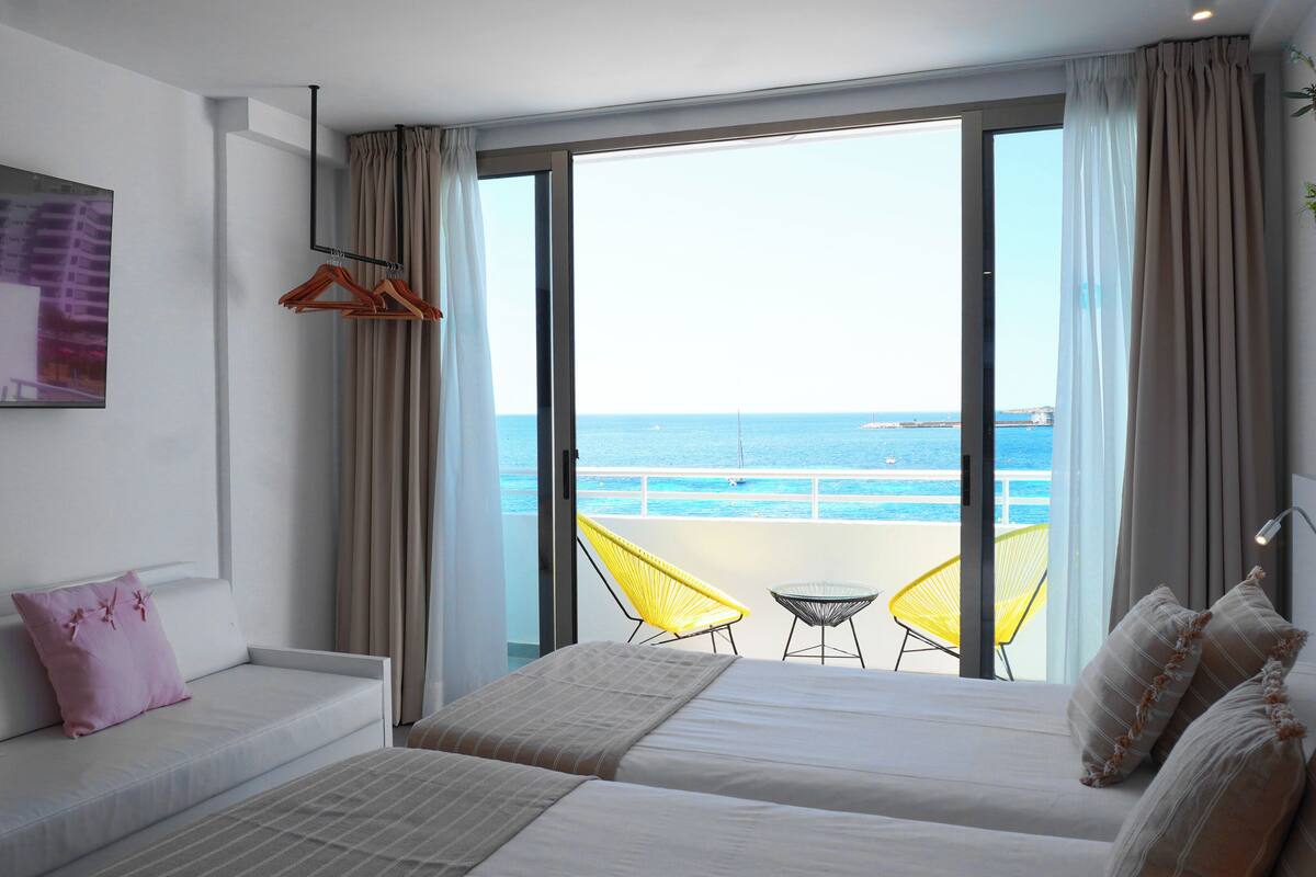 Hotelkamer met een bed, een bank, een televisie en een balkon met uitzicht op zee.