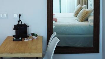 Una habitación con una mesa de madera, una silla, una lámpara colgante y un espejo que refleja una cama con almohadas.