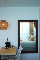 A room with a wooden table, a chair, a hanging light fixture, and a mirror reflecting a bed with pillows.