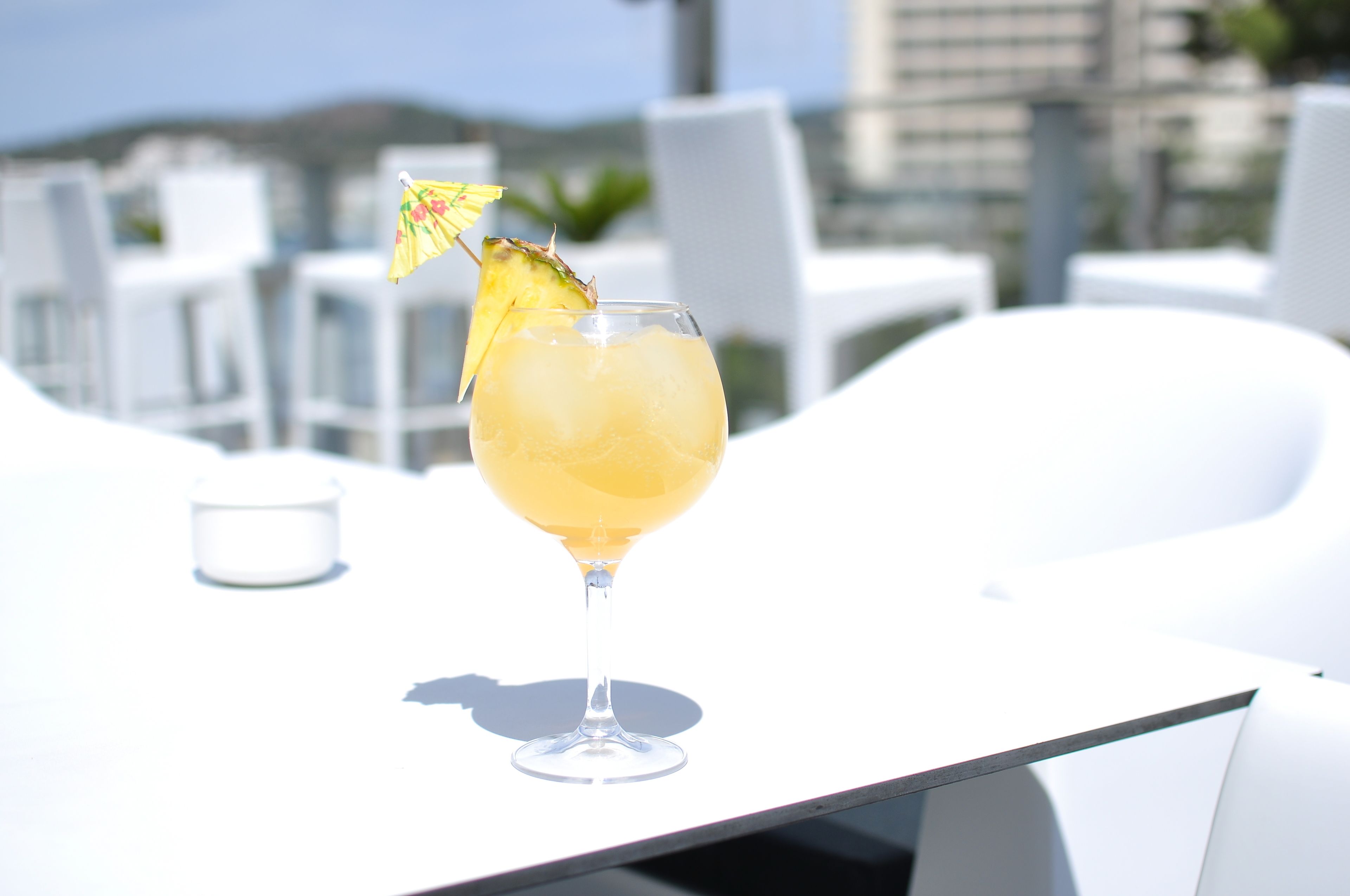 Un vaso de cóctel con un parasol tropical sobre una mesa blanca al aire libre.