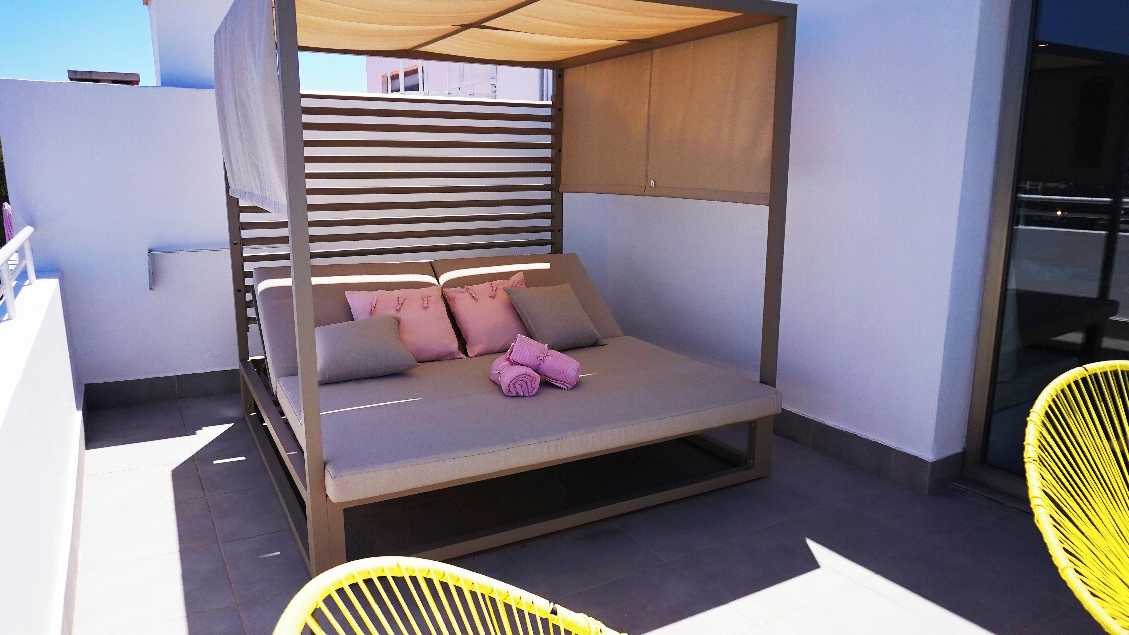 Ein modernes Liegebett im Freien mit Baldachin, Kissen und einem zusammengerollten Handtuch.