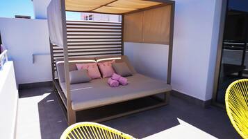 Ein modernes Liegebett im Freien mit Baldachin, Kissen und einem zusammengerollten Handtuch.