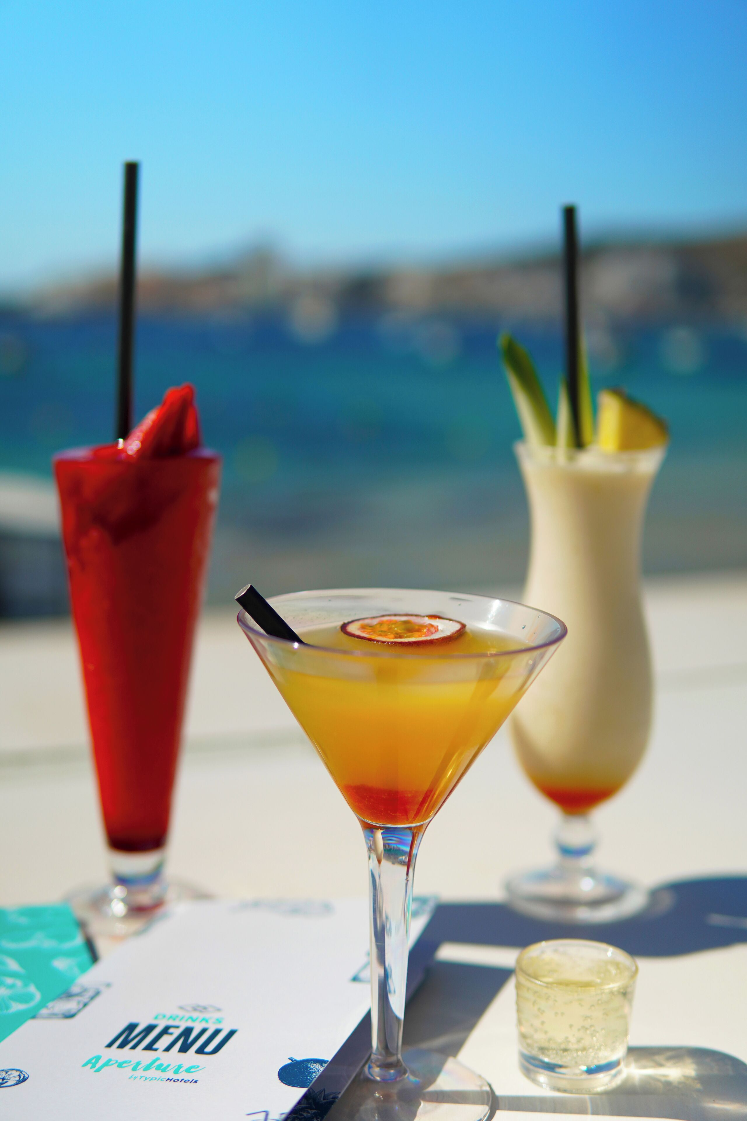 Une table avec trois boissons, un menu et un verre d’eau.