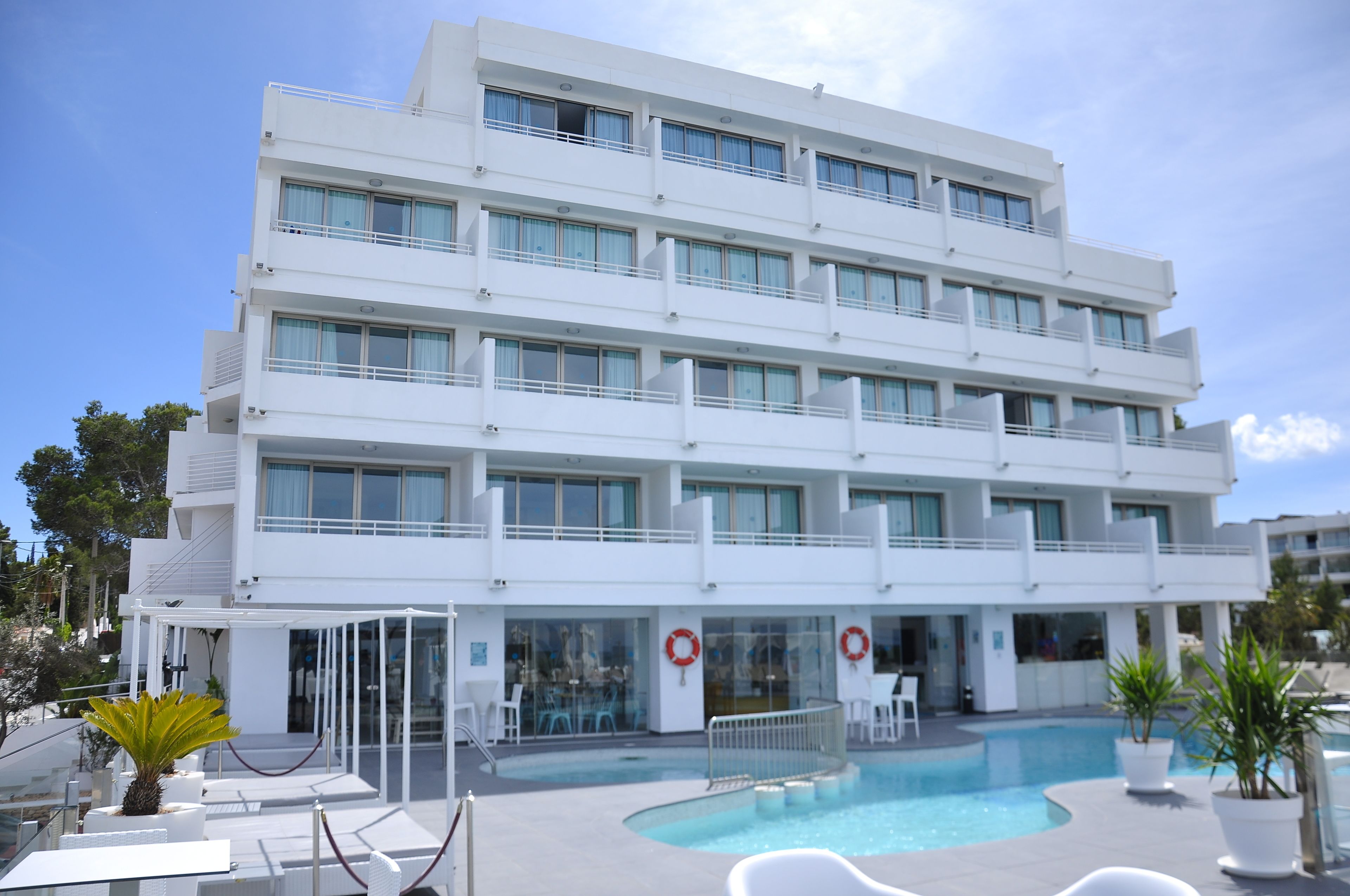 A multi-story hotel with a swimming pool, outdoor seating, and a clear sky.