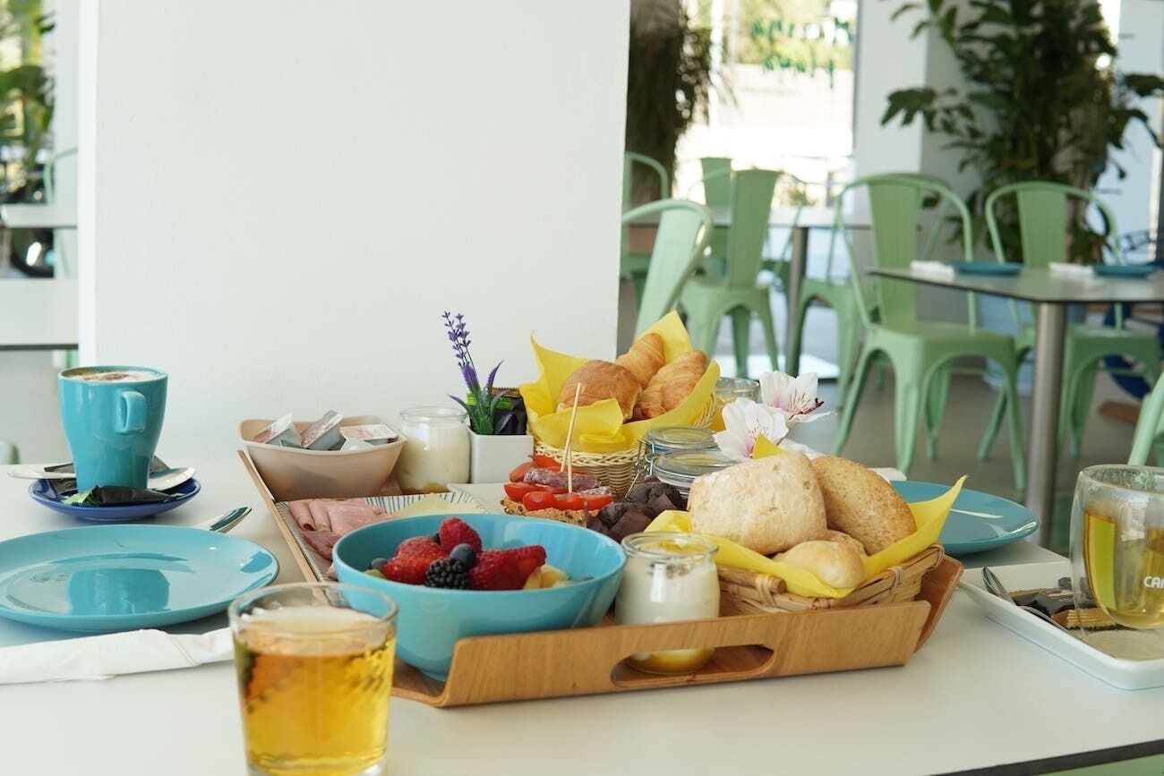A breakfast setting with a tray of croissants, fruits, and pastries, a blue bowl of berries, a glass of tea, and a blue cup on a table.