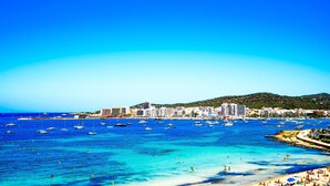 A coastal cityscape with a marina filled with boats, a sandy beach, and a backdrop of buildings. - Marina Playa Hotel Apartments by Typic Hotels – Adults Only (Sant Antoni de Portmany)