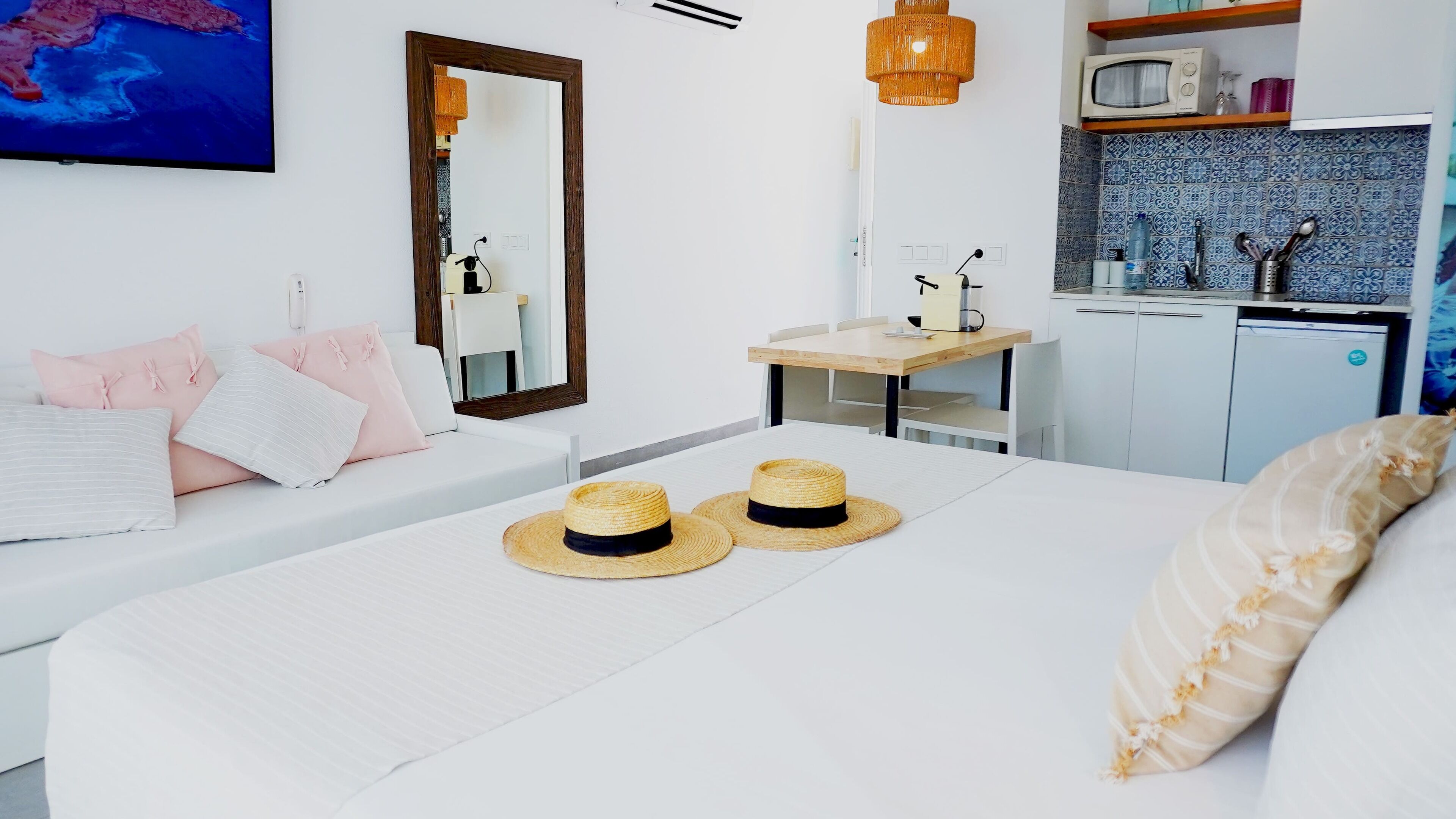 Habitación de hotel moderna con una cama grande, un escritorio pequeño, una kitchenette y un espejo amplio.
