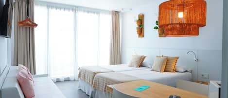 A hotel room with two beds, a desk, a TV, and a large window with curtains.
