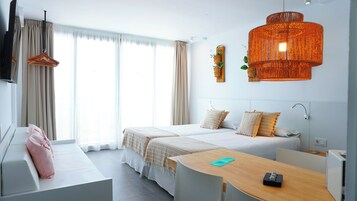 Habitación de hotel con dos camas, un escritorio, televisión y un ventanal grande con cortinas.