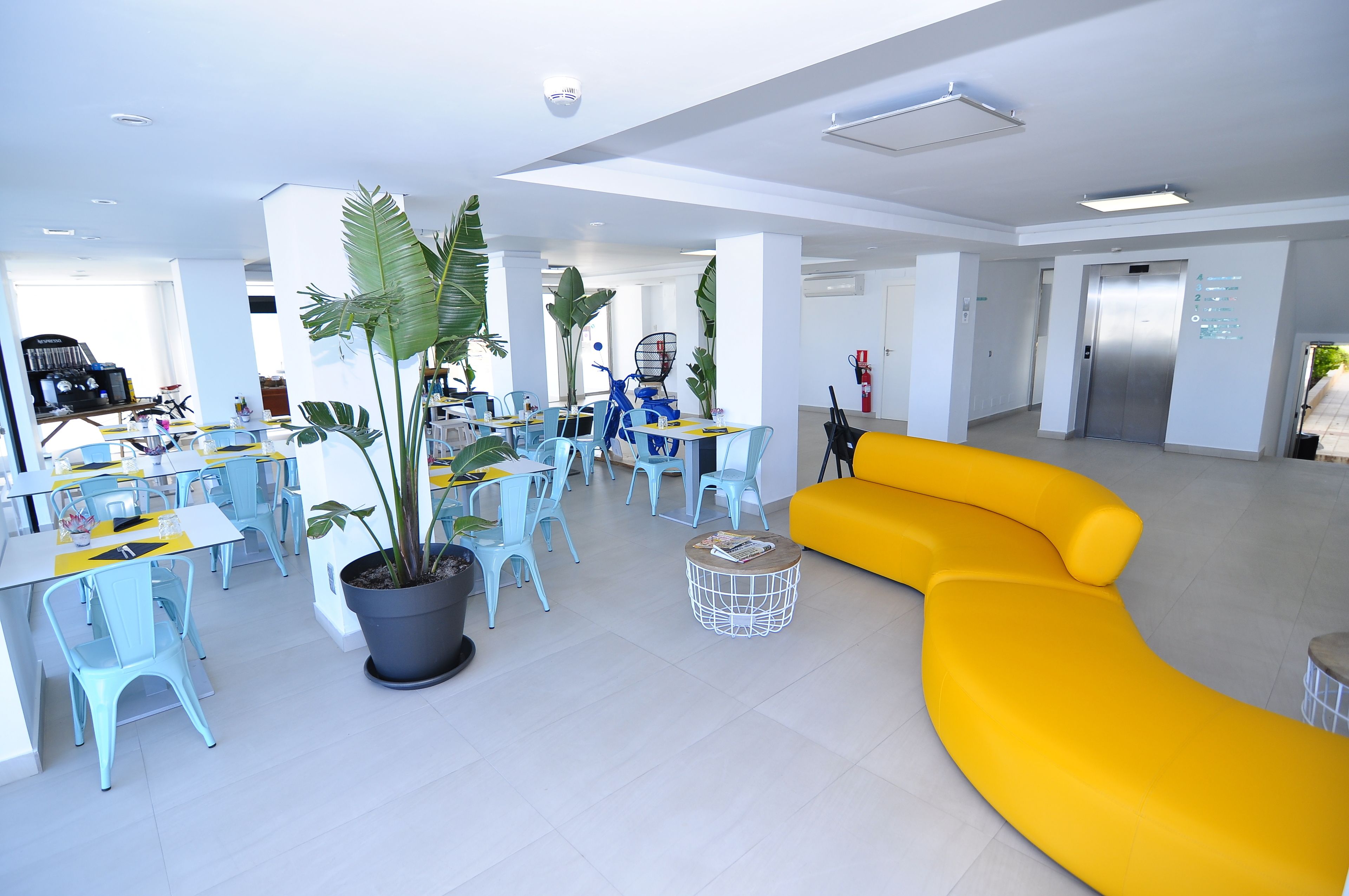 Un espacio interior moderno con zonas de estar, un sofá amarillo y plantas en macetas.