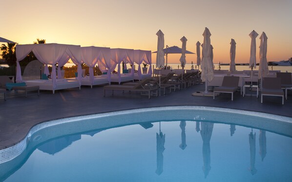 Ein Poolbereich mit Liegestühlen und Sonnenschirmen, ein klares Schwimmbecken und Blick auf einen Sonnenuntergang.