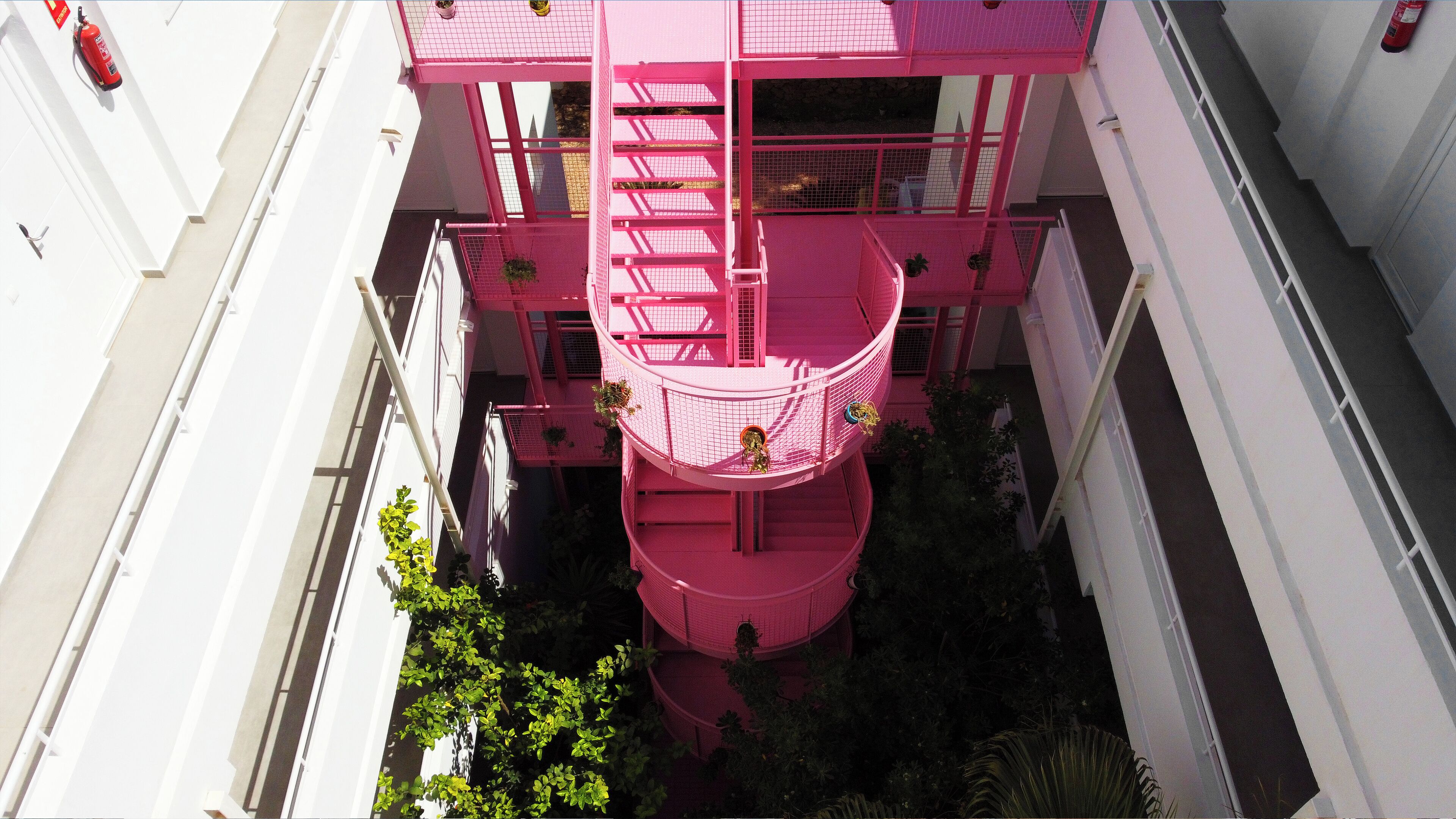 A multi-level pink building with balconies, staircases, and potted plants.