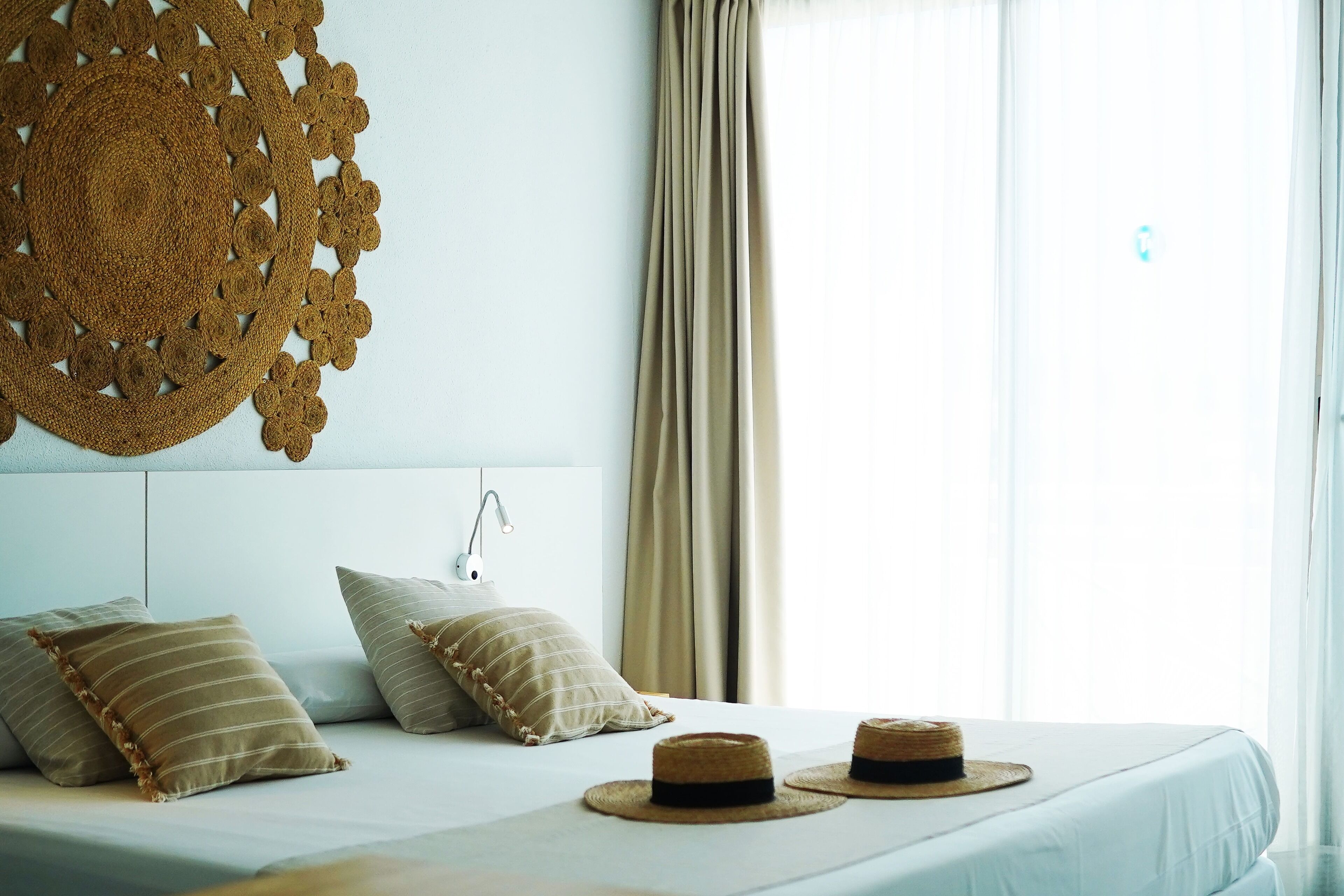 Een netjes opgemaakt bed met twee kussens, een geweven wanddecoratie en twee strooihutten op het bed.